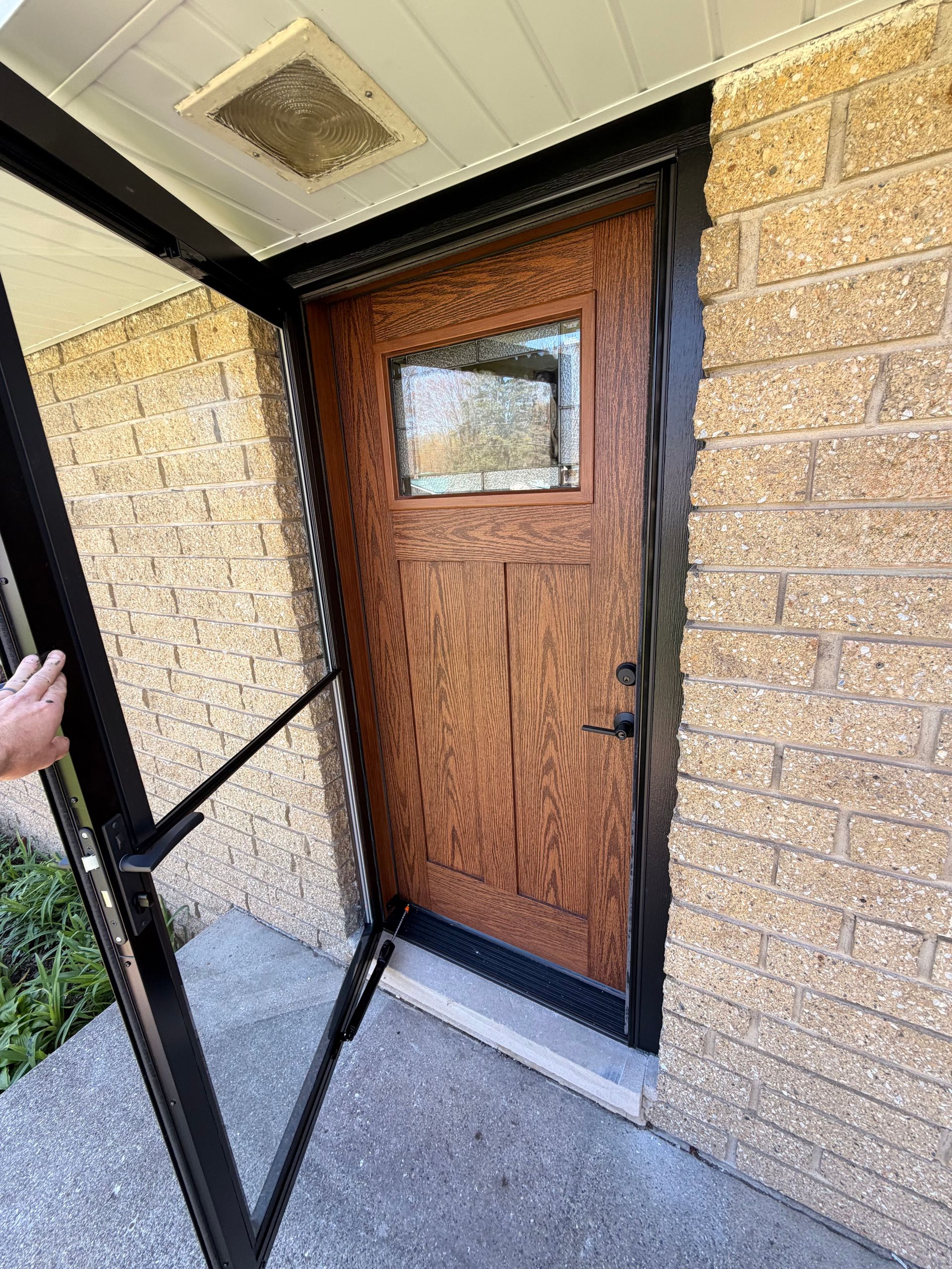Front porch entry with a wooden door, small window, and open screen door beside brick walls.