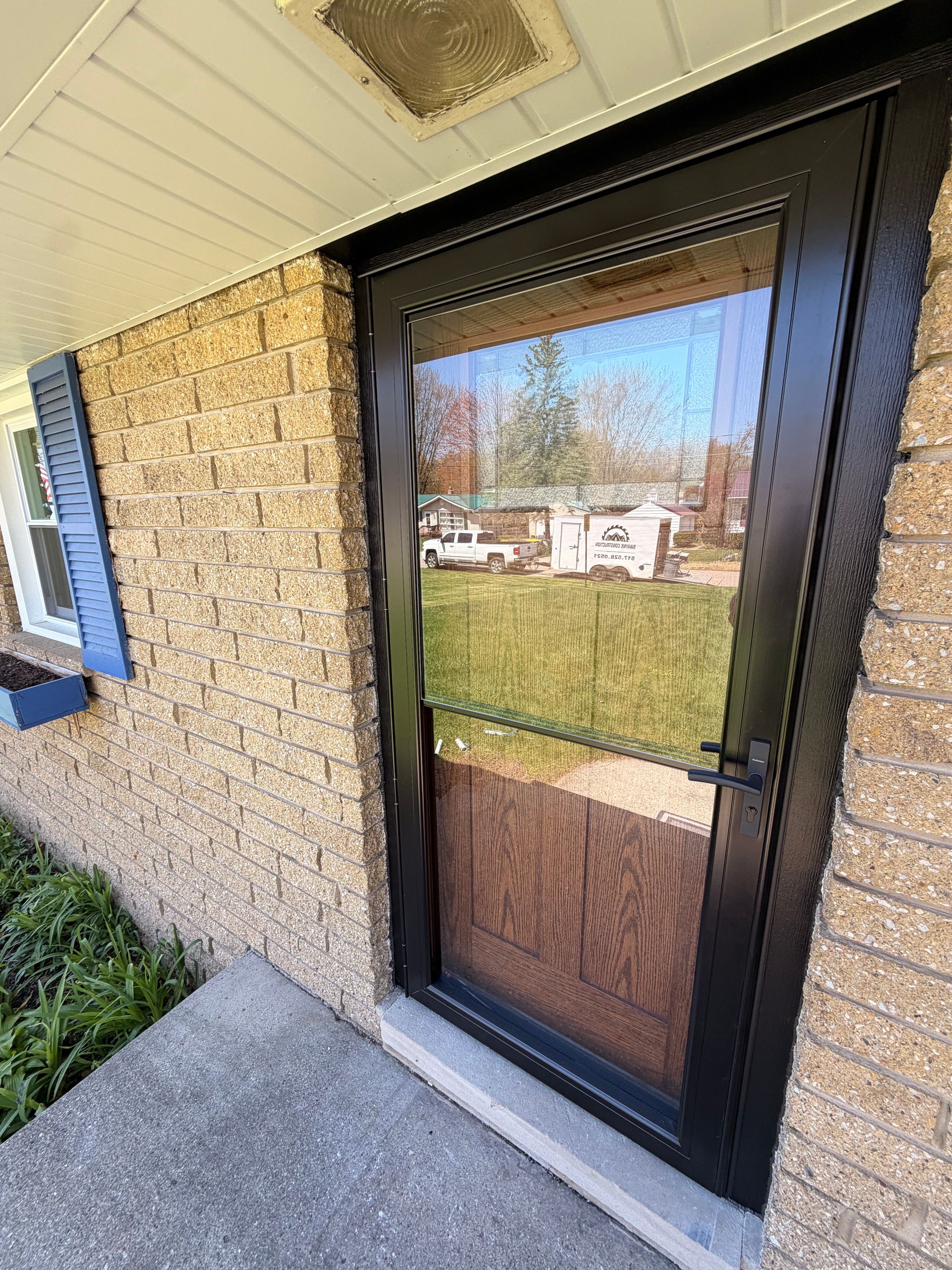 Front entry with a black screen door, tan brick wall, and concrete porch overlooking a grassy yard.