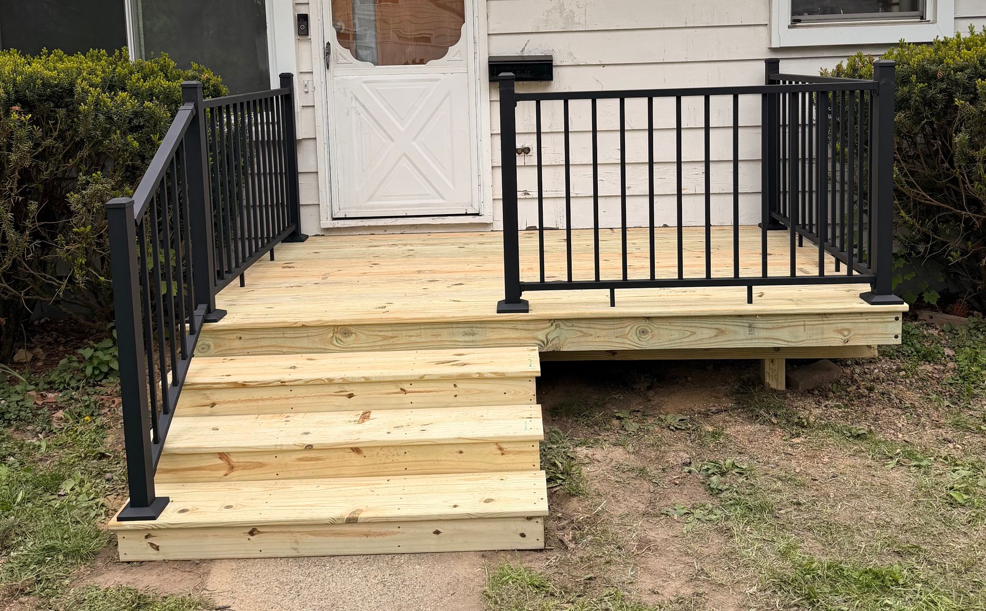 Wooden ramp with black railings leading to a front porch and white door