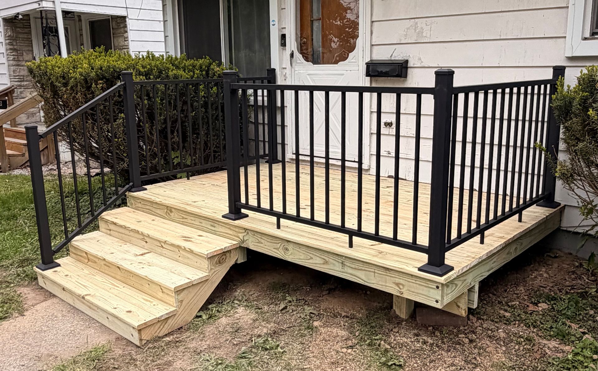 Small raised porch with black railing and beige steps on a house exterior.