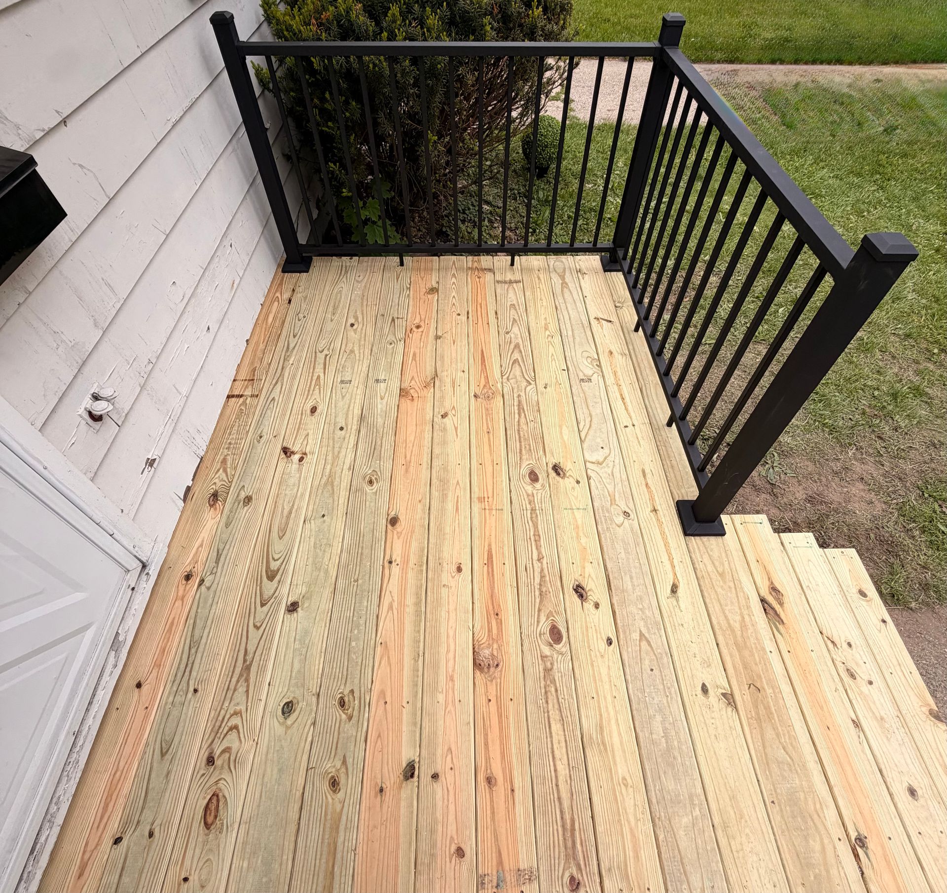 Wooden porch deck with black railings and steps beside a house.
