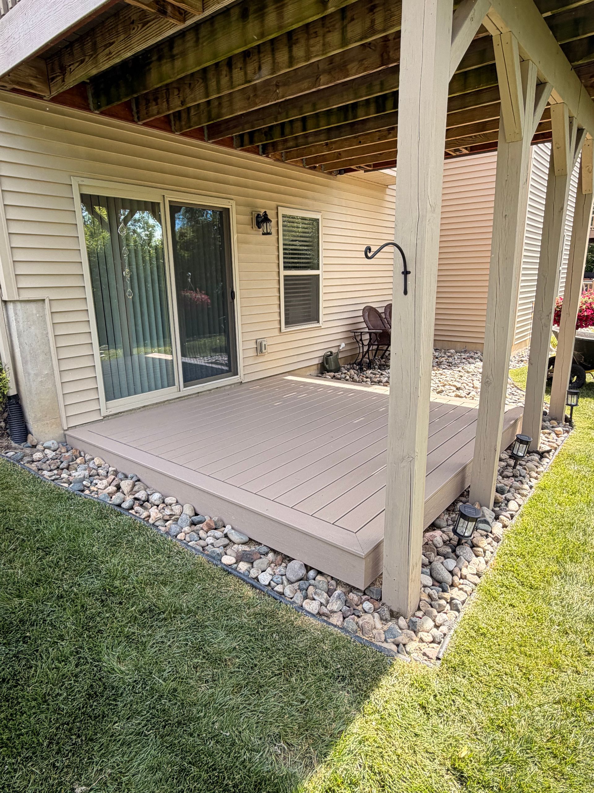 Covered patio with beige flooring, sliding glass door, and wooden posts beside a grassy yard