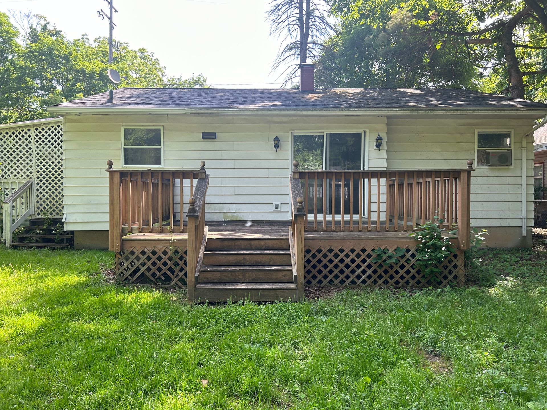Small white house with a wooden front porch and steps, surrounded by a grassy yard and trees.