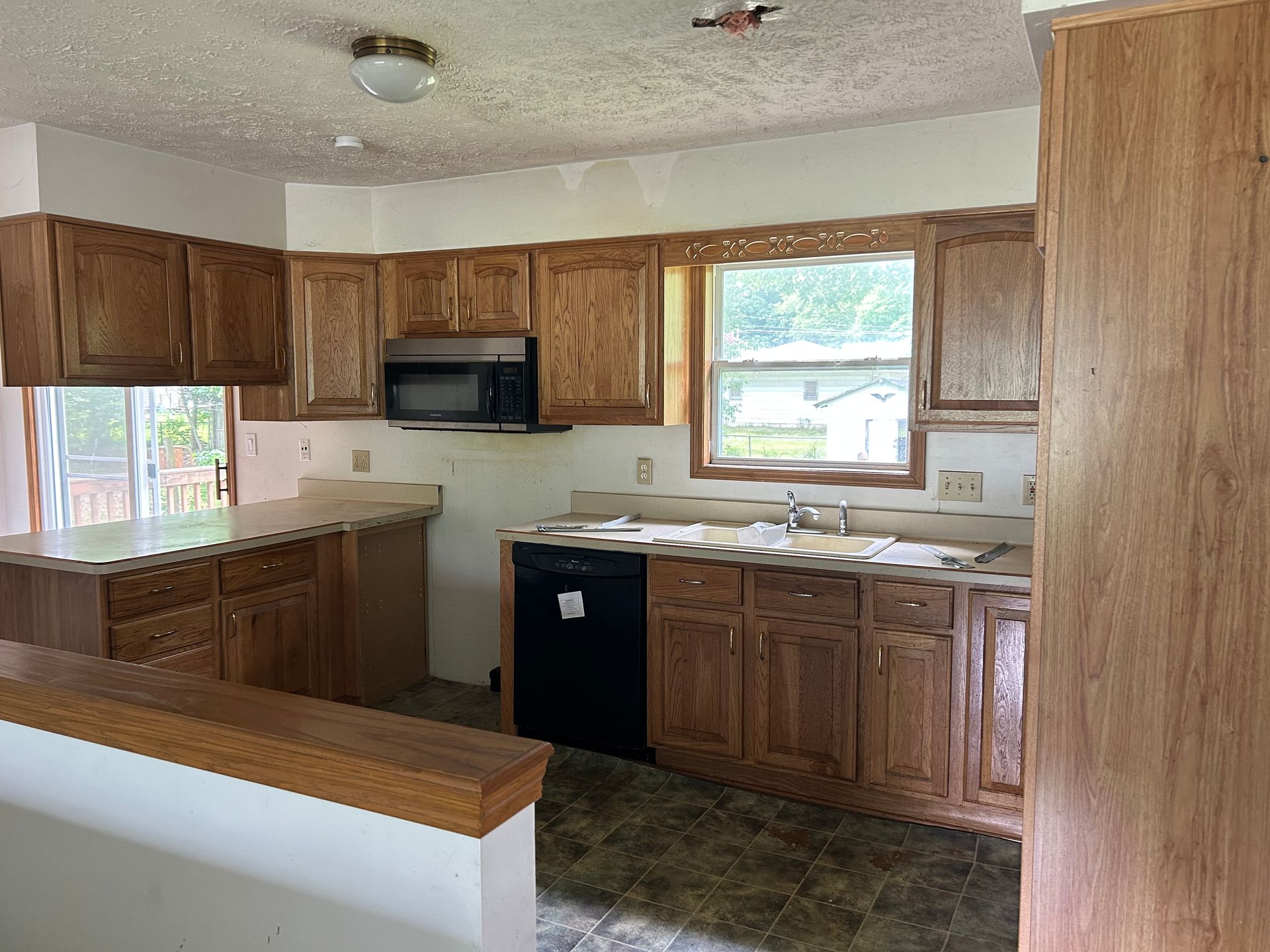 Empty kitchen with wood cabinets, beige walls, black appliances, and a window over the sink