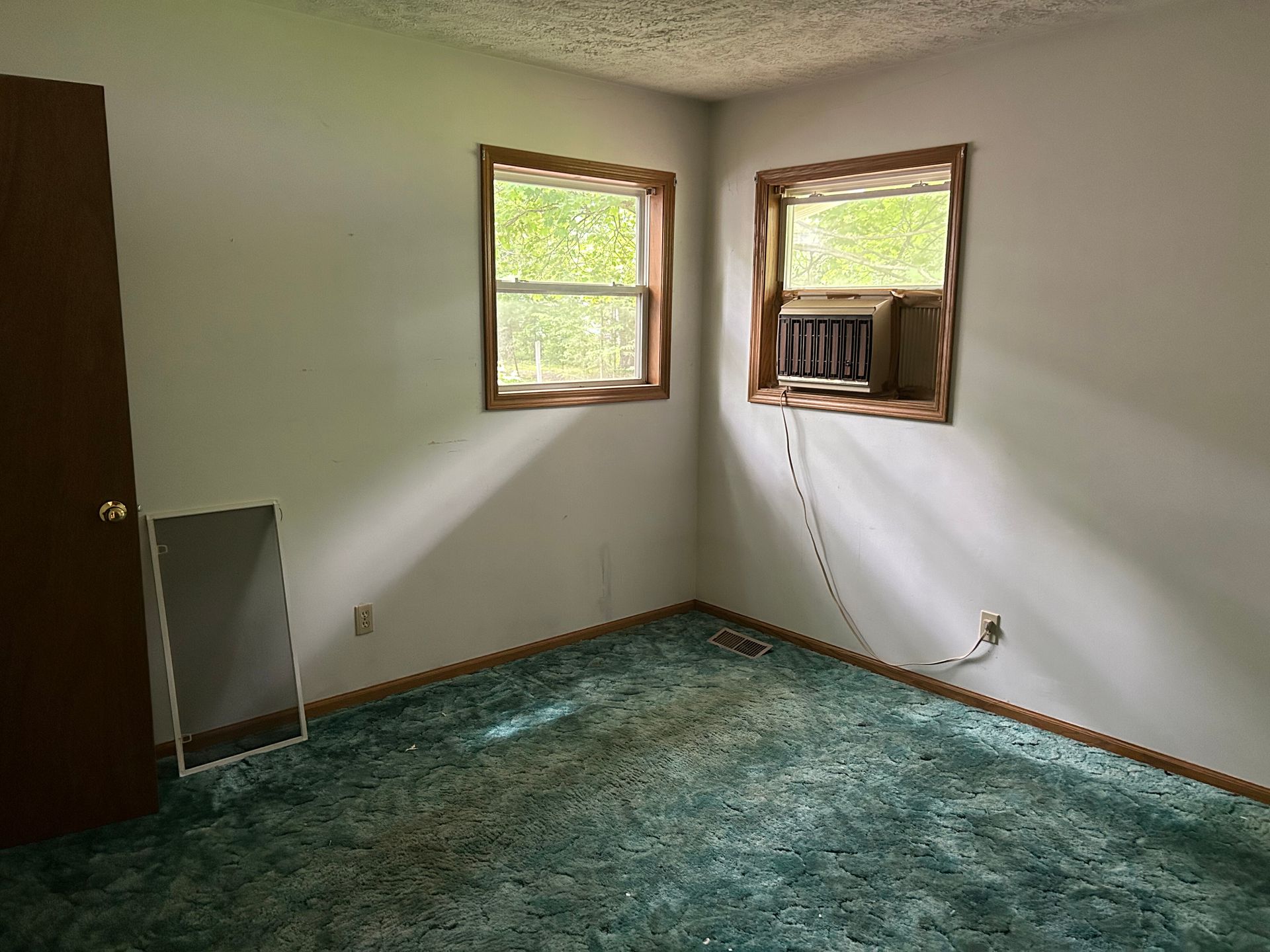 Empty room with teal carpet, white walls, two windows, and a window air conditioner unit