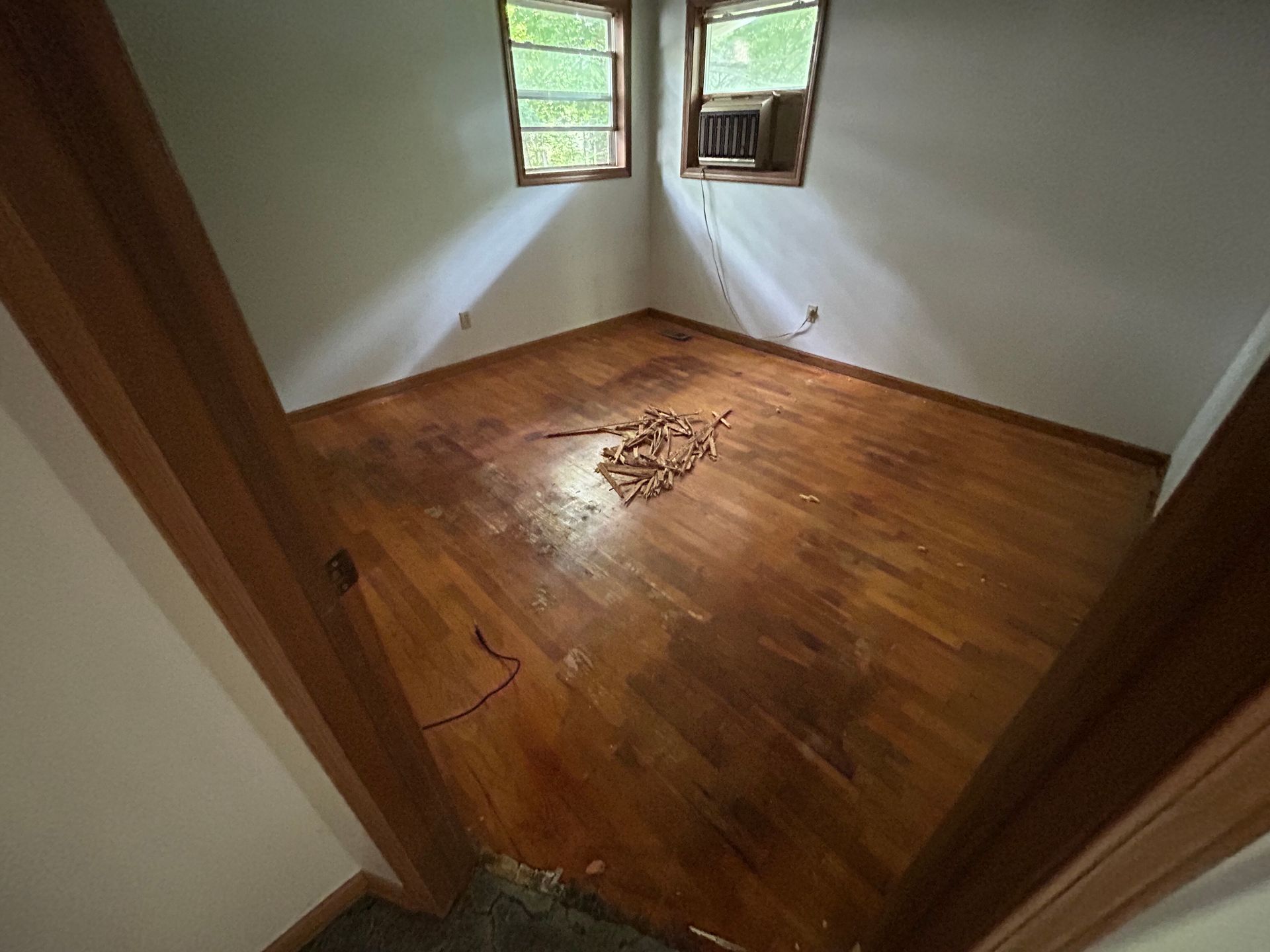 Empty room with wooden floor, white walls, and two small windows.