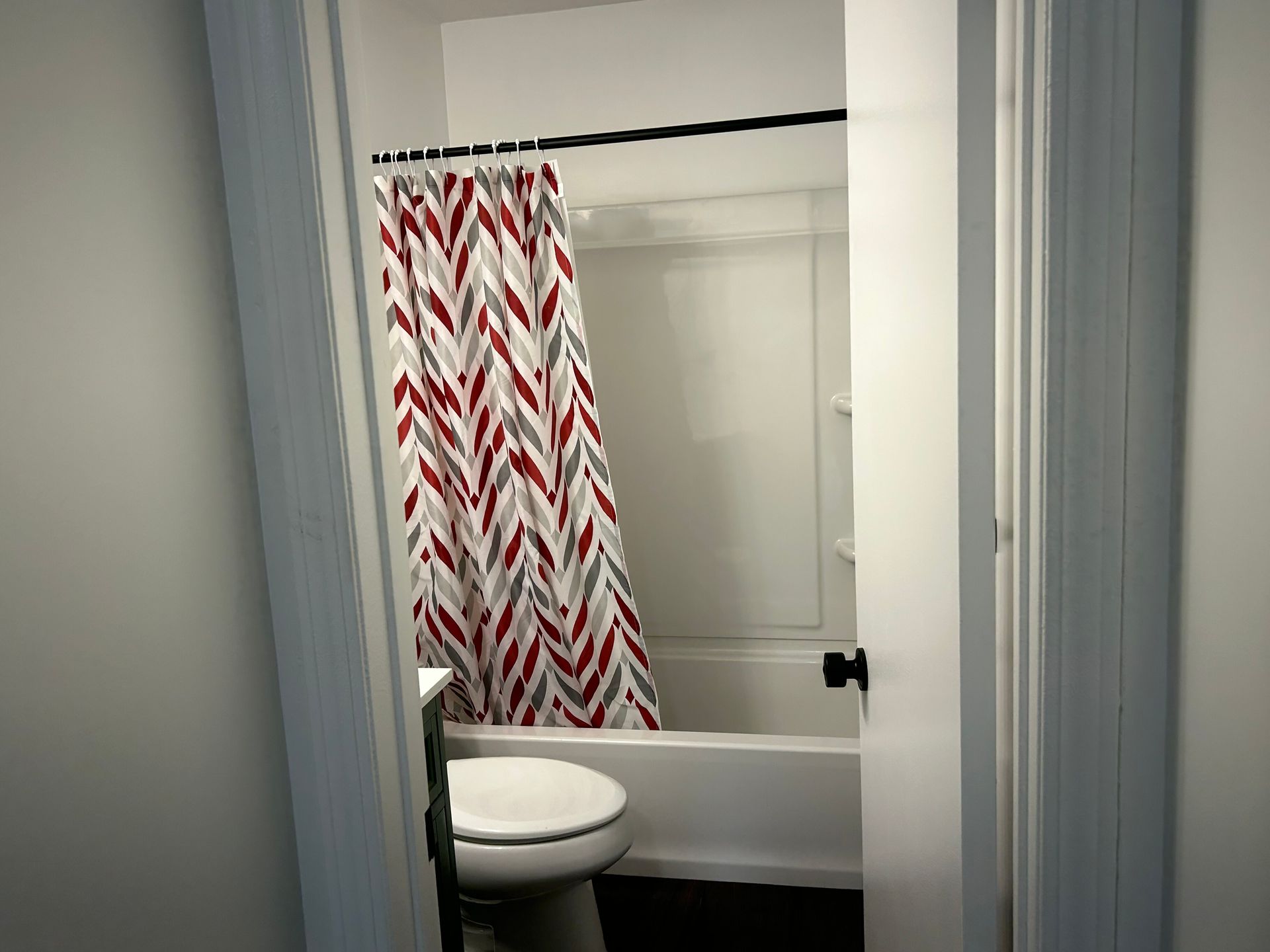 Bathroom with a toilet, bathtub, and red-and-white patterned shower curtain.