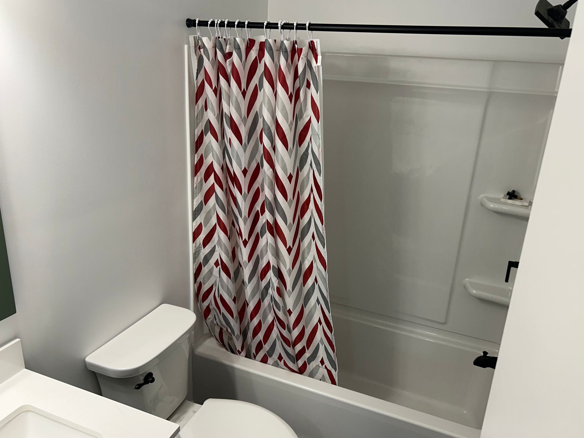 Bathroom with white shower curtain patterned in red and gray chevrons, toilet, and tiled tub area