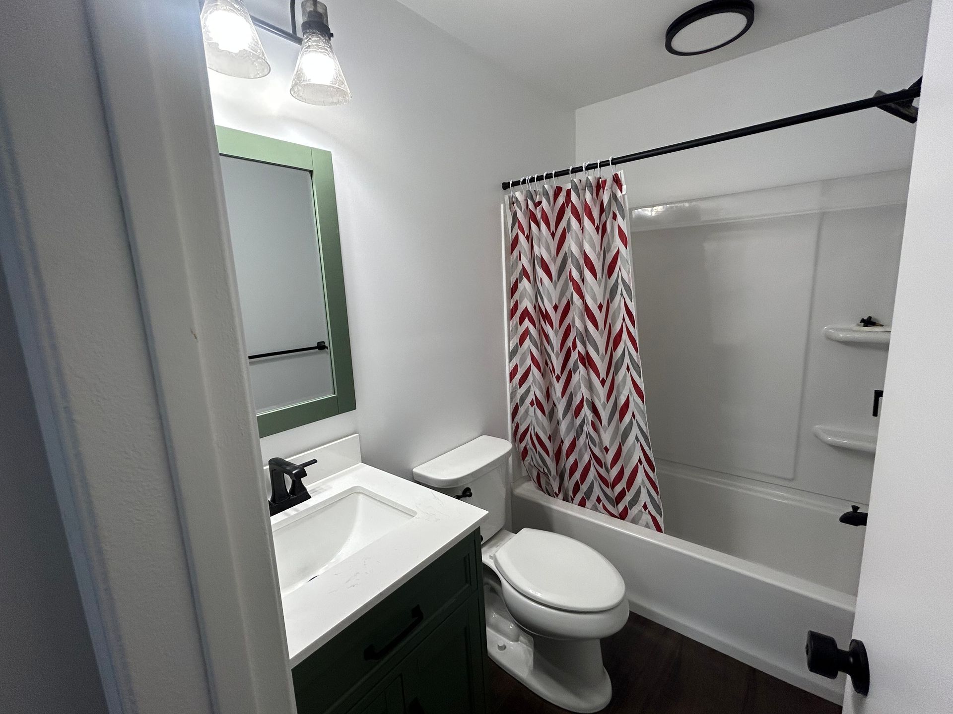 Small bathroom with sink, toilet, shower-tub, and red chevron curtain