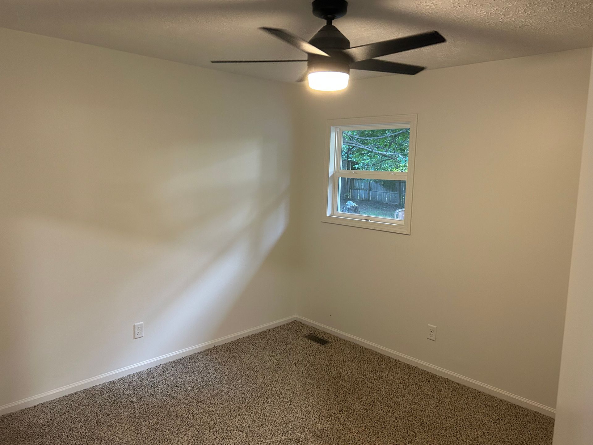 Empty beige bedroom with carpet, ceiling fan, and small window.