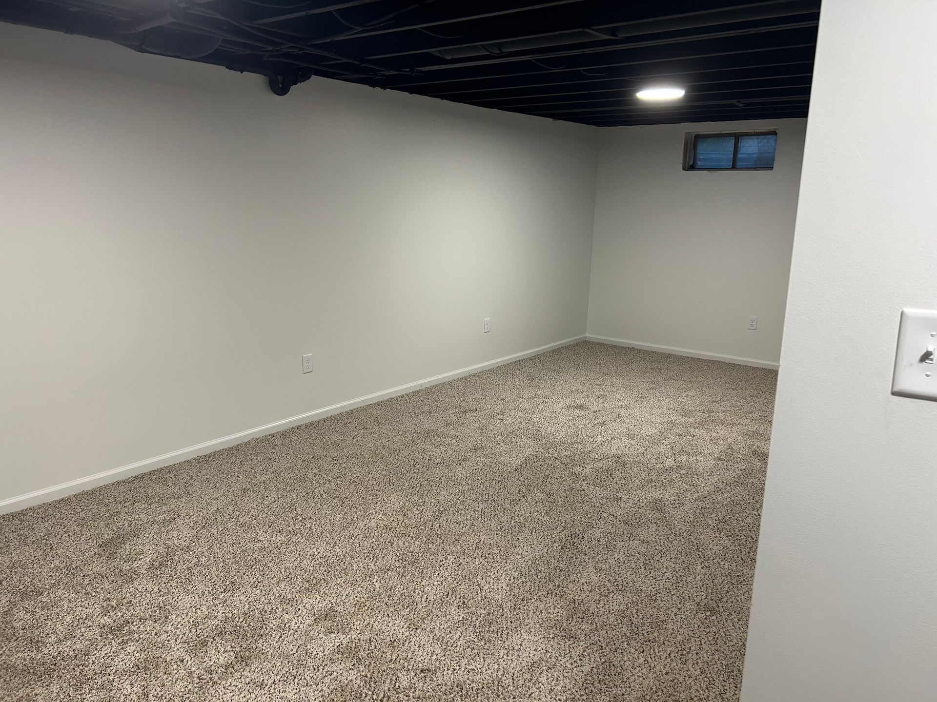 Empty carpeted room with white walls and dark ceiling, viewed toward a back corner