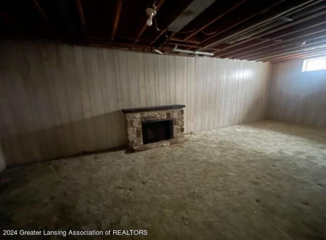 Empty unfinished basement with a stone fireplace and exposed ceiling beams.