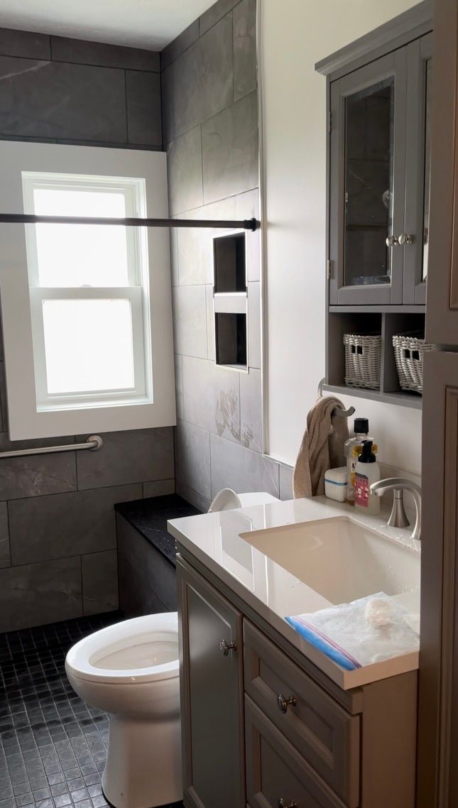 Small bathroom with gray walls, window, shower curtain rod, and dark wood vanity with sink.