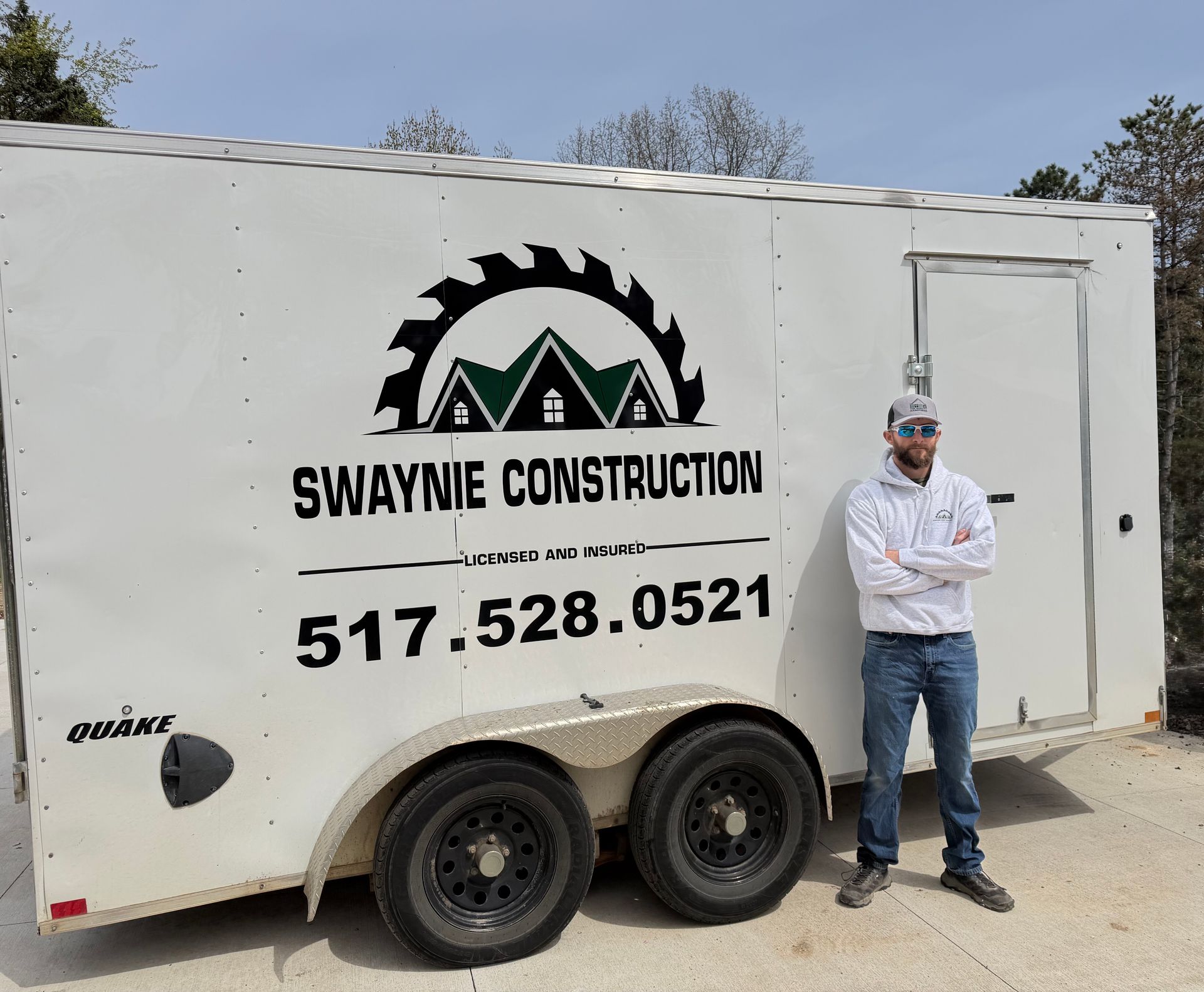 Swaynie Construction trailer with logo, phone number, and a man standing beside it outdoors