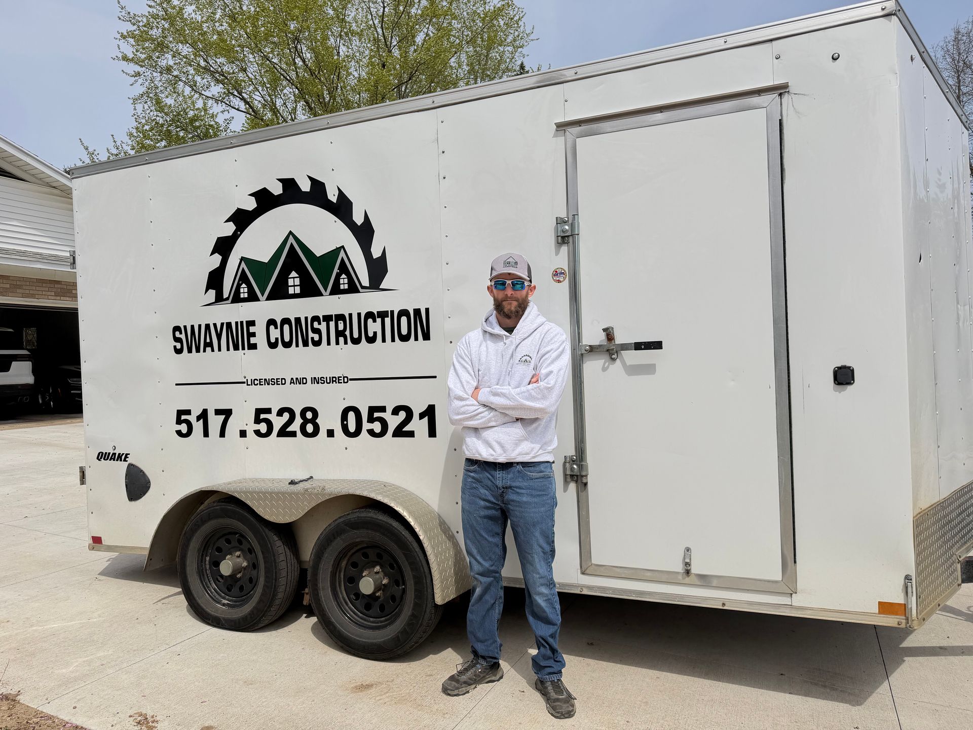 Man standing beside white construction trailer with logo and phone number on the side