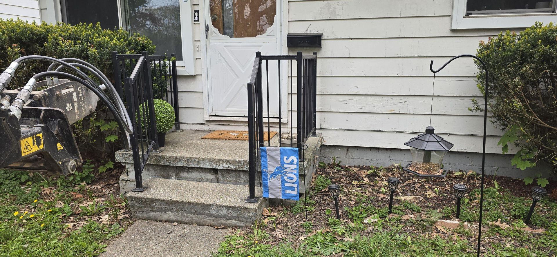 House front steps with a black handrail, small garden, and blue sign by the entrance