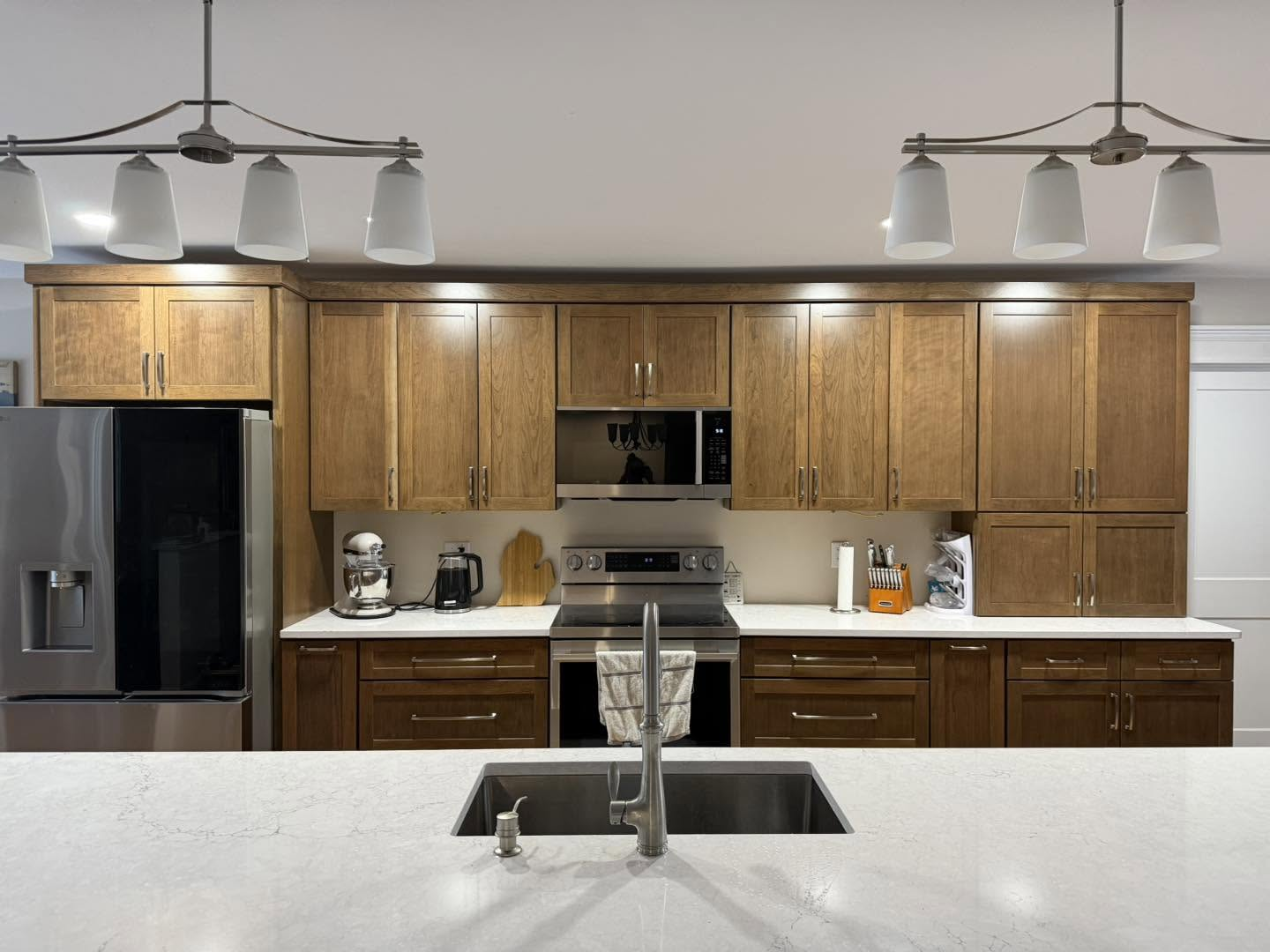 Modern kitchen with wood cabinets, stainless appliances, and a white island sink under pendant lights