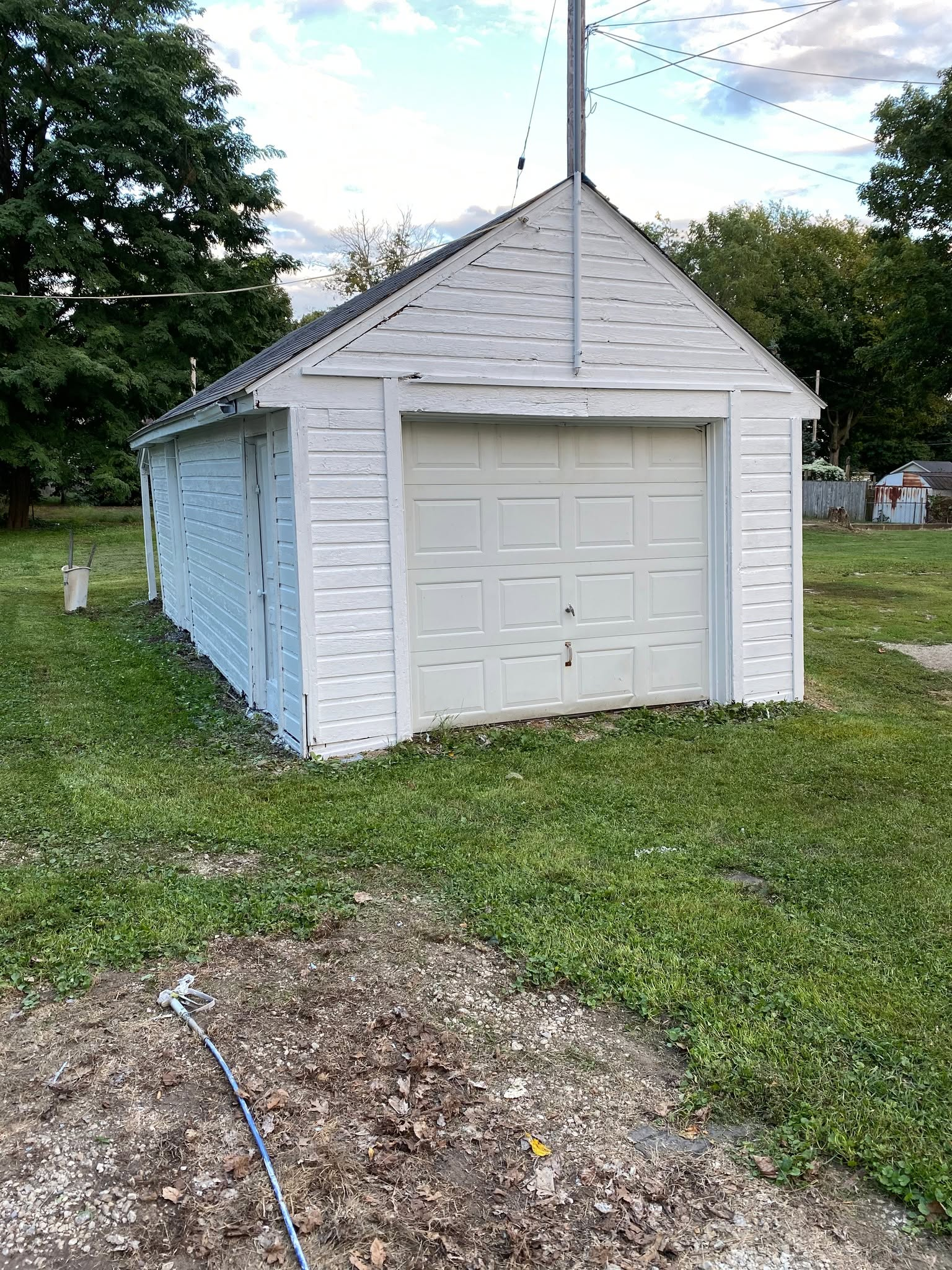 White garage with a single door and antenna in a grassy yard, with trees and a cloudy sky.