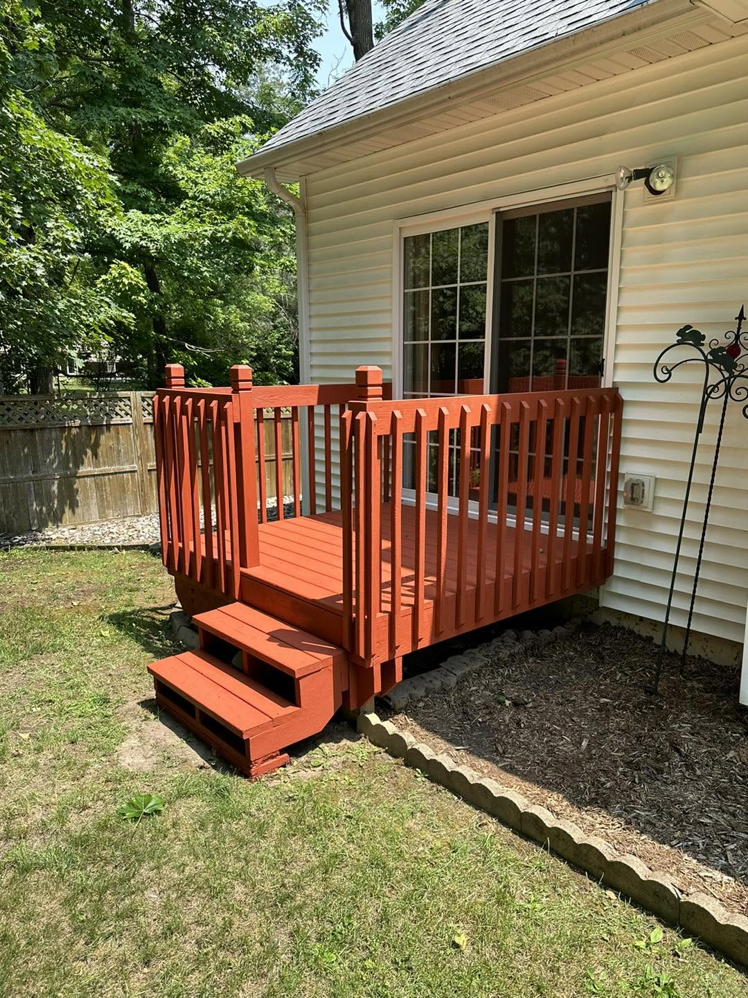 Small red wooden porch deck with steps beside a beige house in a sunny backyard