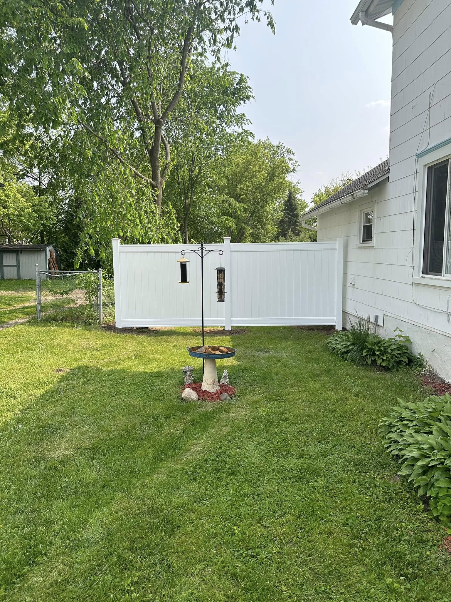 Backyard with green lawn, white fence, and a bird feeder near a white house