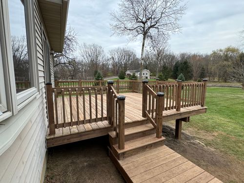Covered backyard patio with wooden posts, sliding glass door, and gravel edging beside a lawn.
