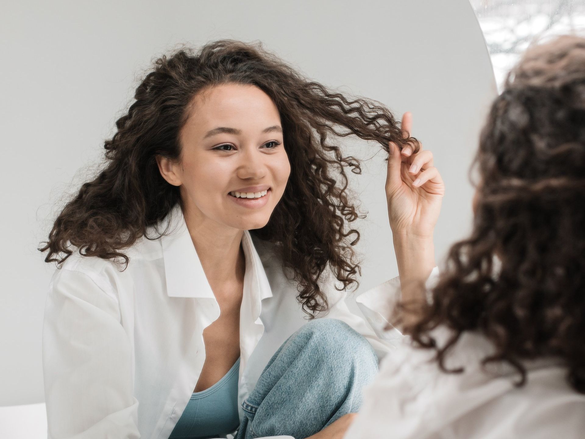 woman holing curly hair looking in the mirror