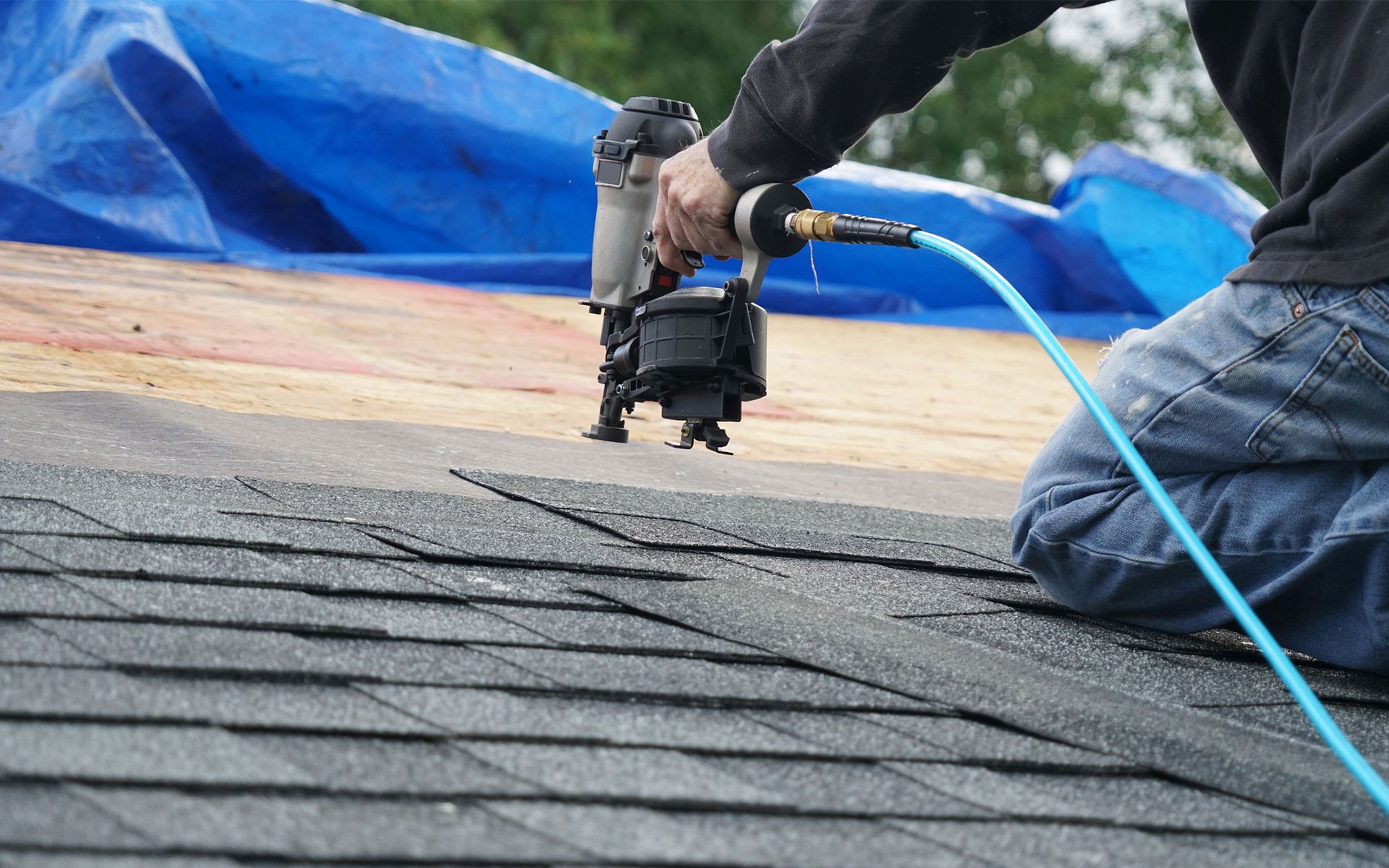 A handyman using nail gun to install shingle to repair roof