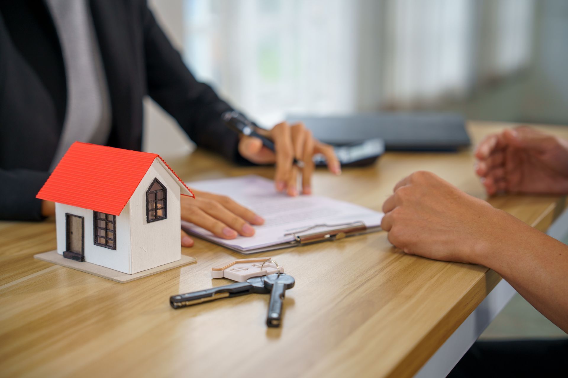 Real estate meeting with house model, keys, and paperwork on a desk