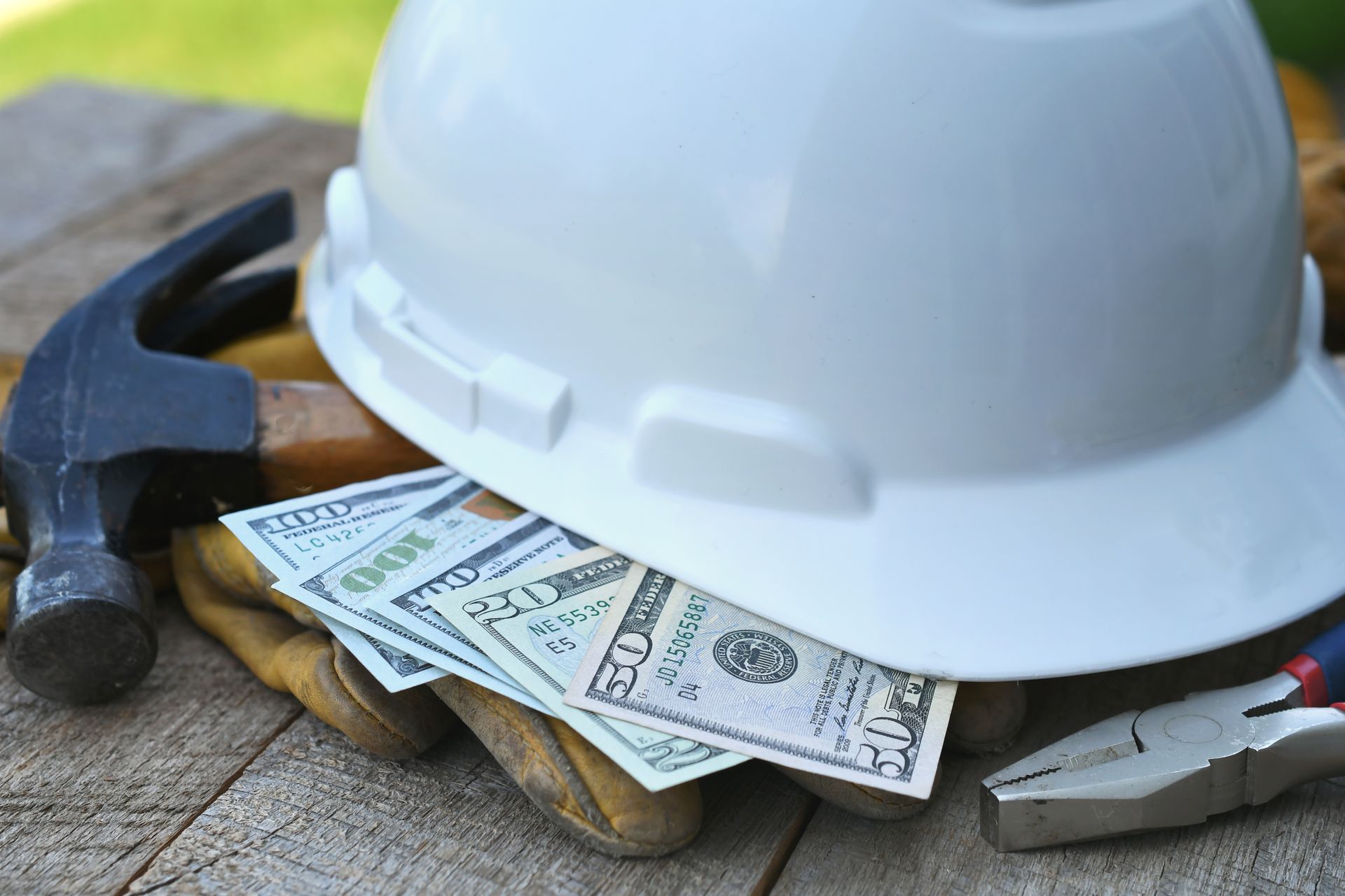 Construction hard hat, hammer, gloves, and cash on a wooden surface