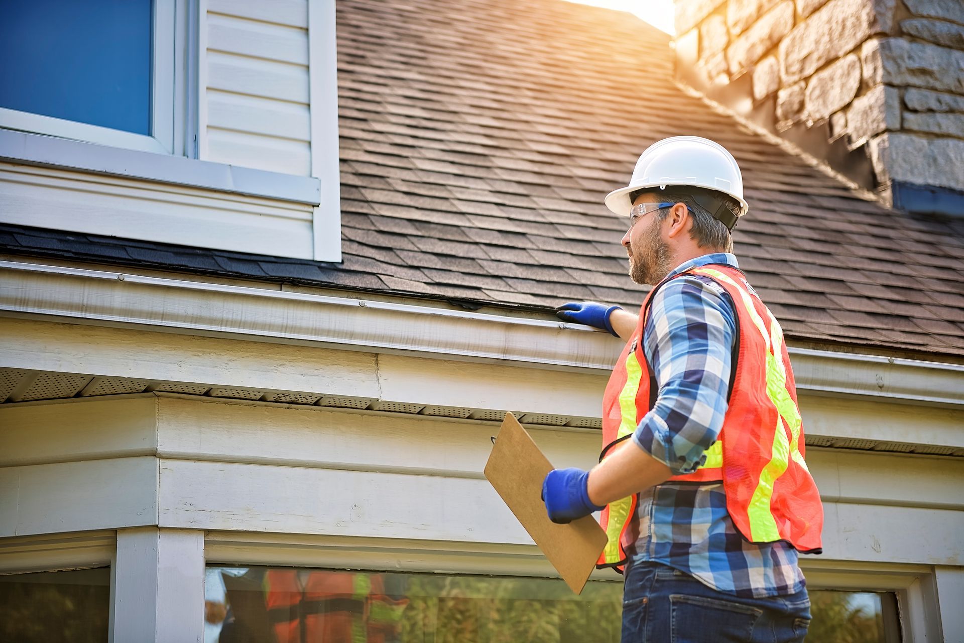 Home inspector in hard hat and safety vest examining a house exterior with clipboard