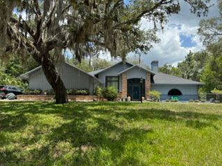 Gray suburban house with a large front lawn and a sprawling oak tree in the yard