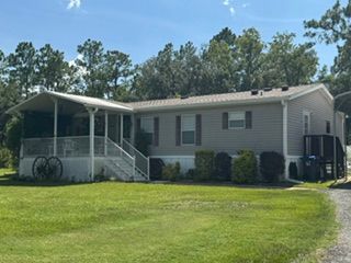 Single-story mobile home with a covered porch, front steps, and a large green lawn under a blue sky