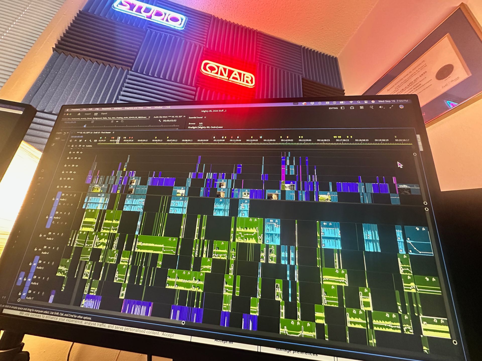 A computer monitor shows a colorful software timeline in a dim room with neon wall signs above it