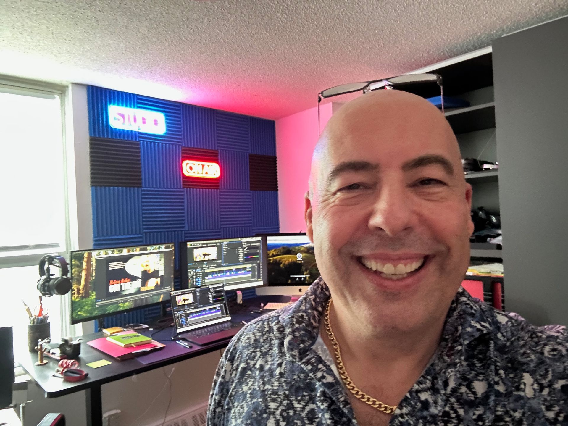 Smiling man in home studio with dual monitors, colorful LED signs, and acoustic foam walls