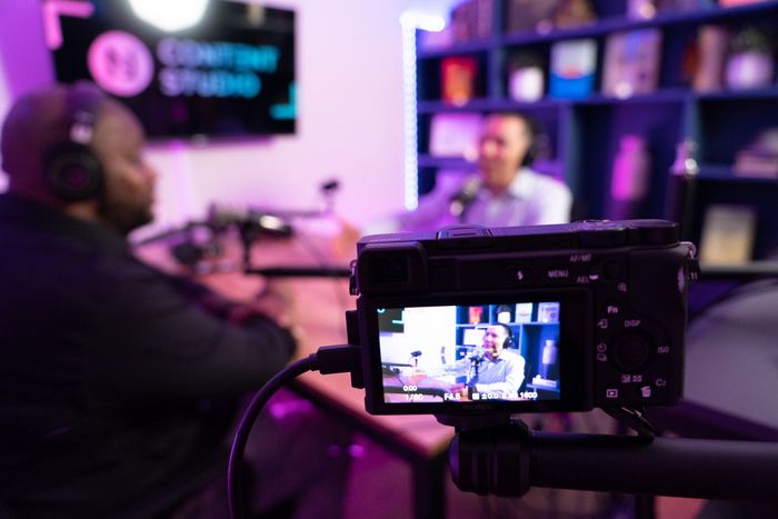 A camera is recording a man talking into a microphone in a studio.