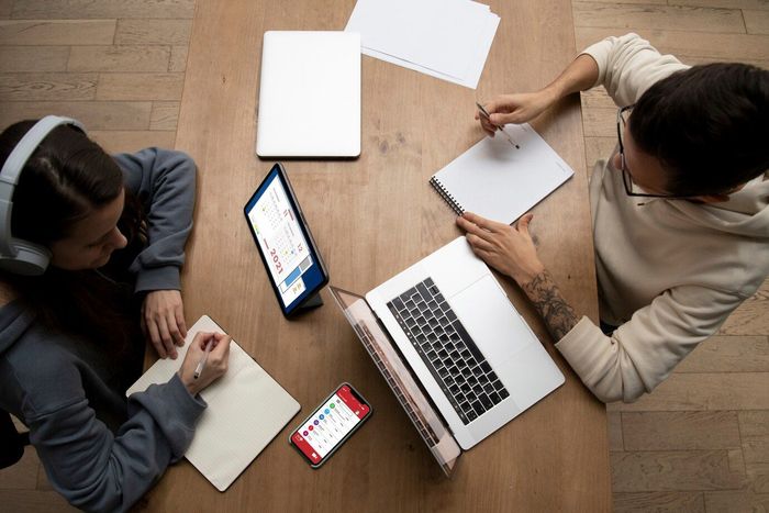 A group of people are sitting around a table with laptops and tablets.