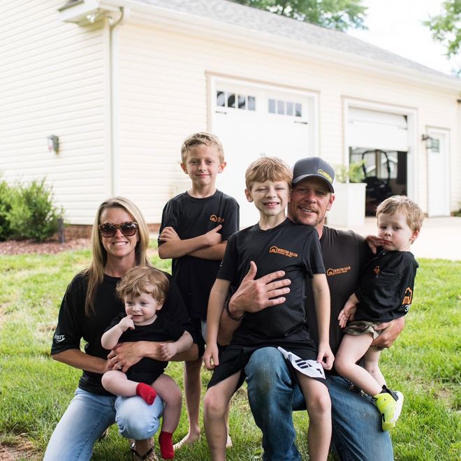 Family of five sitting together on the lawn in front of a white house, smiling at the camera