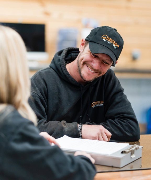 Smiling man in black hoodie and cap talking across a table in a bright workshop