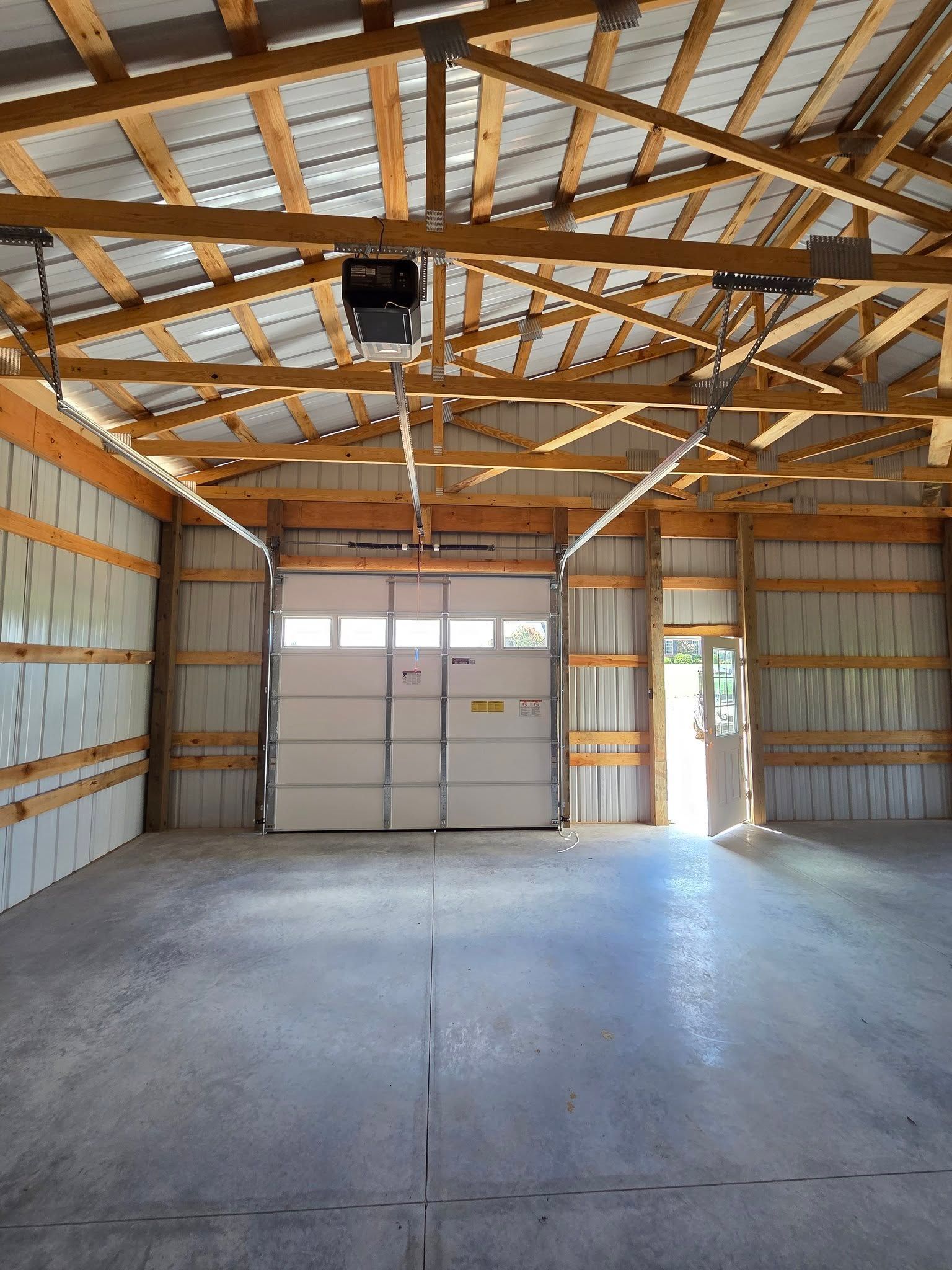 Empty garage interior with concrete floor, exposed wooden rafters, and a large closed door.