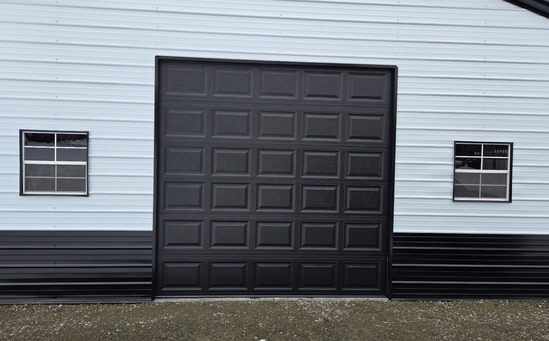 Black garage door centered on a light gray building with two small windows on either side