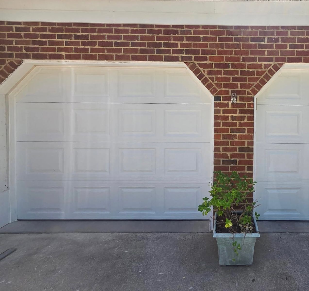 White garage doors on a brick building with a potted plant in front of the center pillar