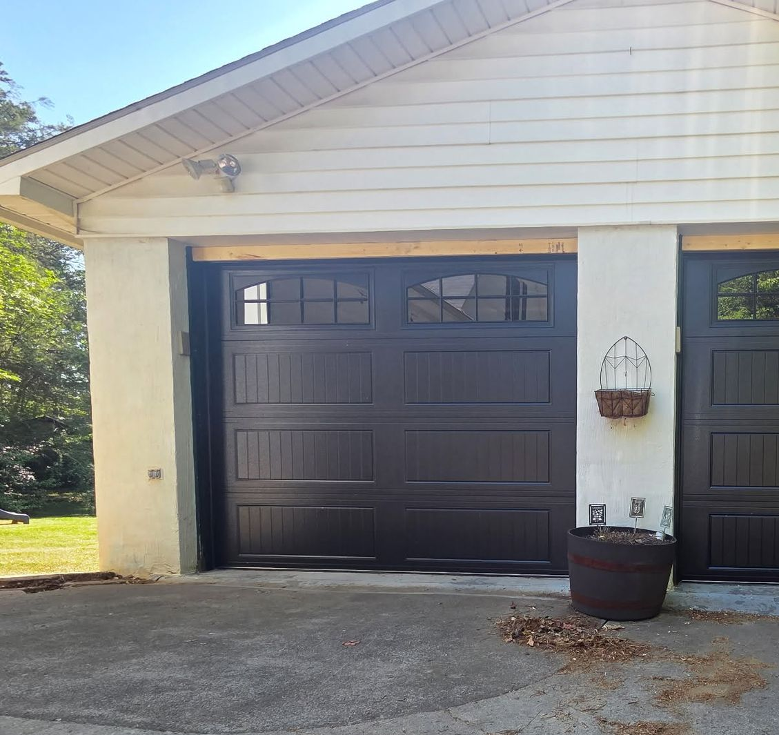 House exterior with a dark garage door, white siding, and a hanging planter beside the driveway