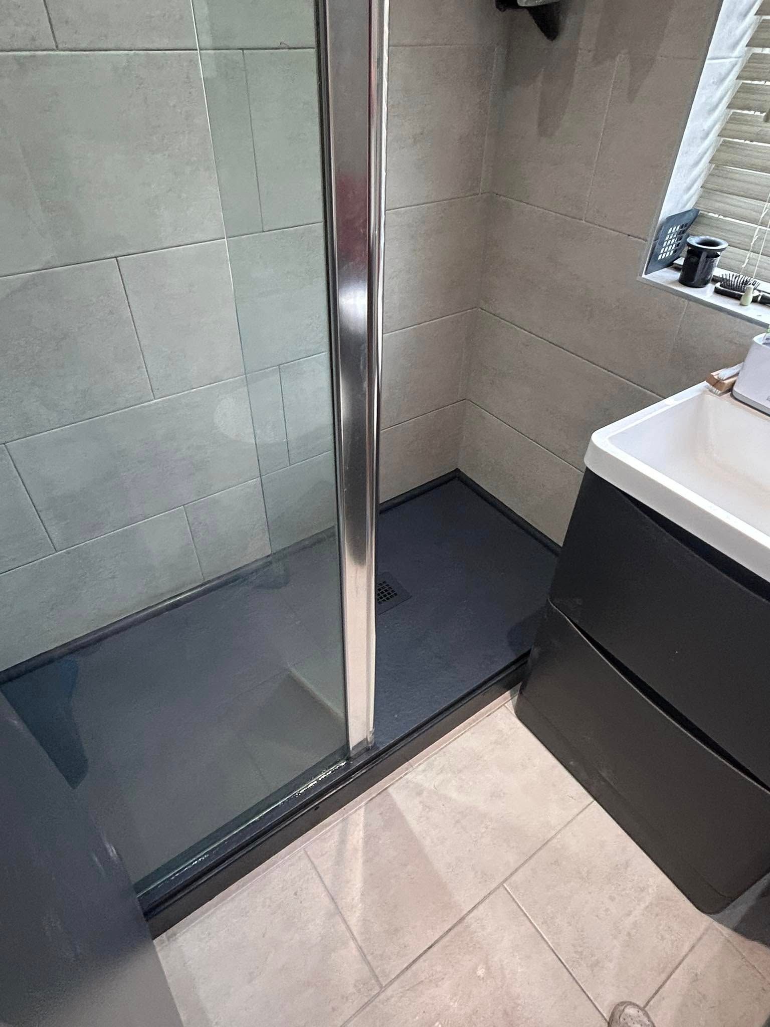 Glass shower enclosure with chrome trim beside a white sink in a tiled bathroom.