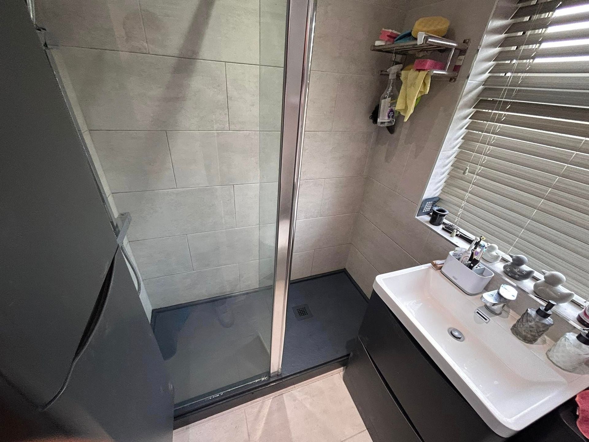 Small bathroom with tiled shower stall, sink, and window blinds.