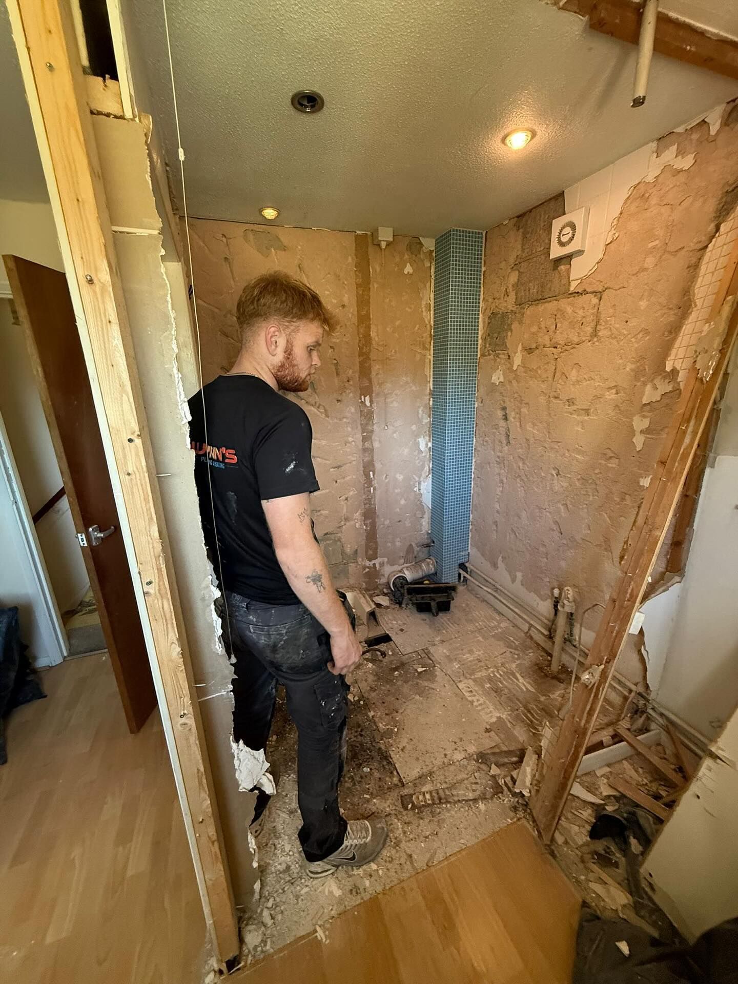 Worker in a small bathroom under renovation, standing amid exposed walls and construction debris.