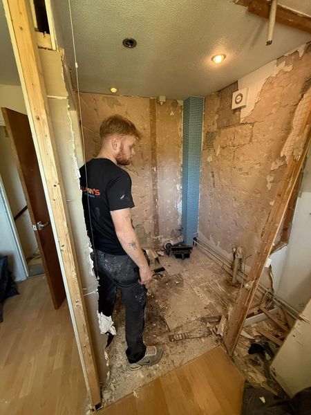 Worker in a narrow room under renovation, surrounded by exposed walls and construction debris.