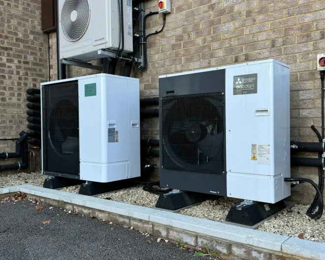 Two outdoor HVAC heat pump units beside a brick building on a gravel strip.