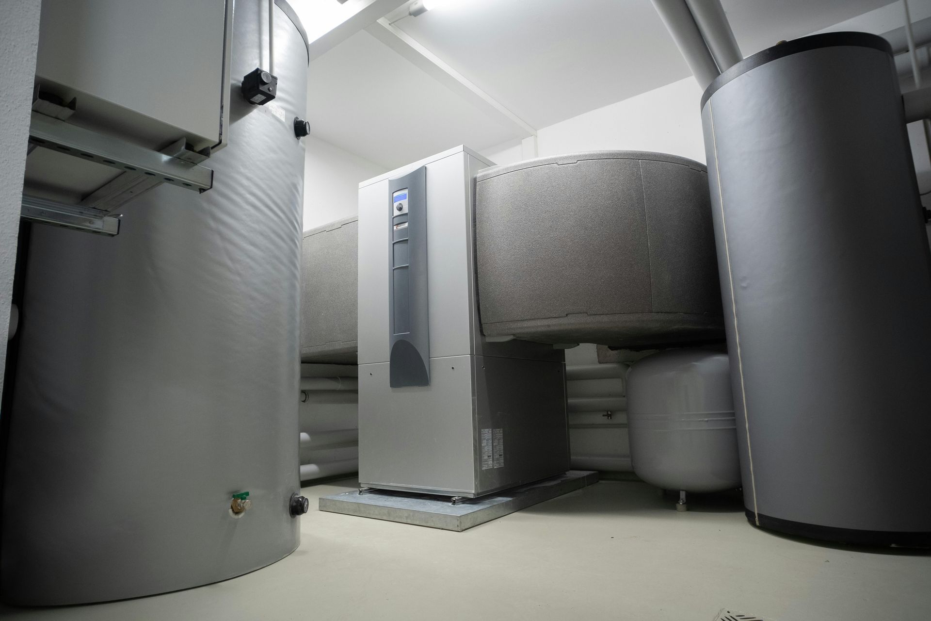 Industrial room with large gray tanks and a central control unit in a mechanical basement area