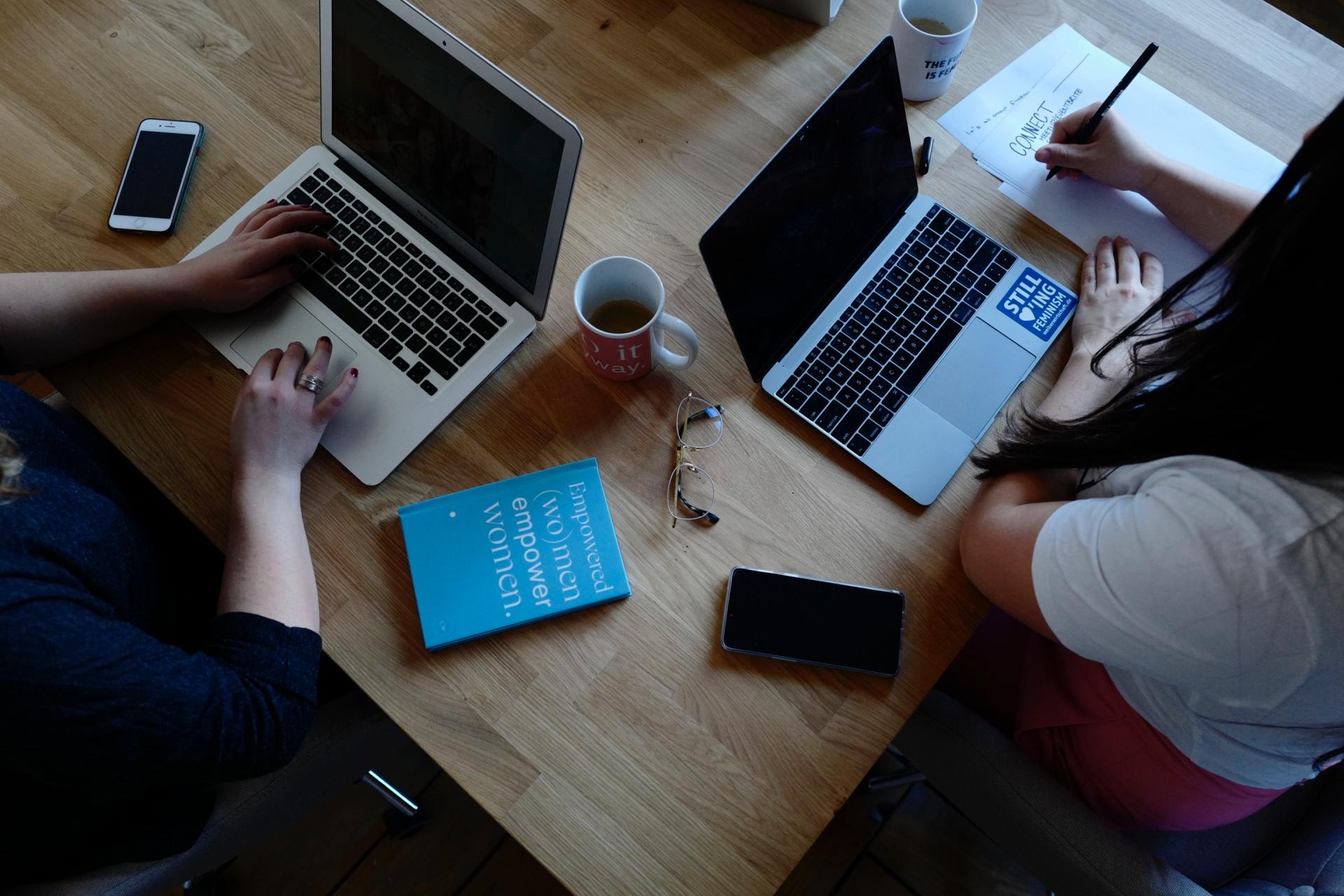Two people are sitting at a table using laptops