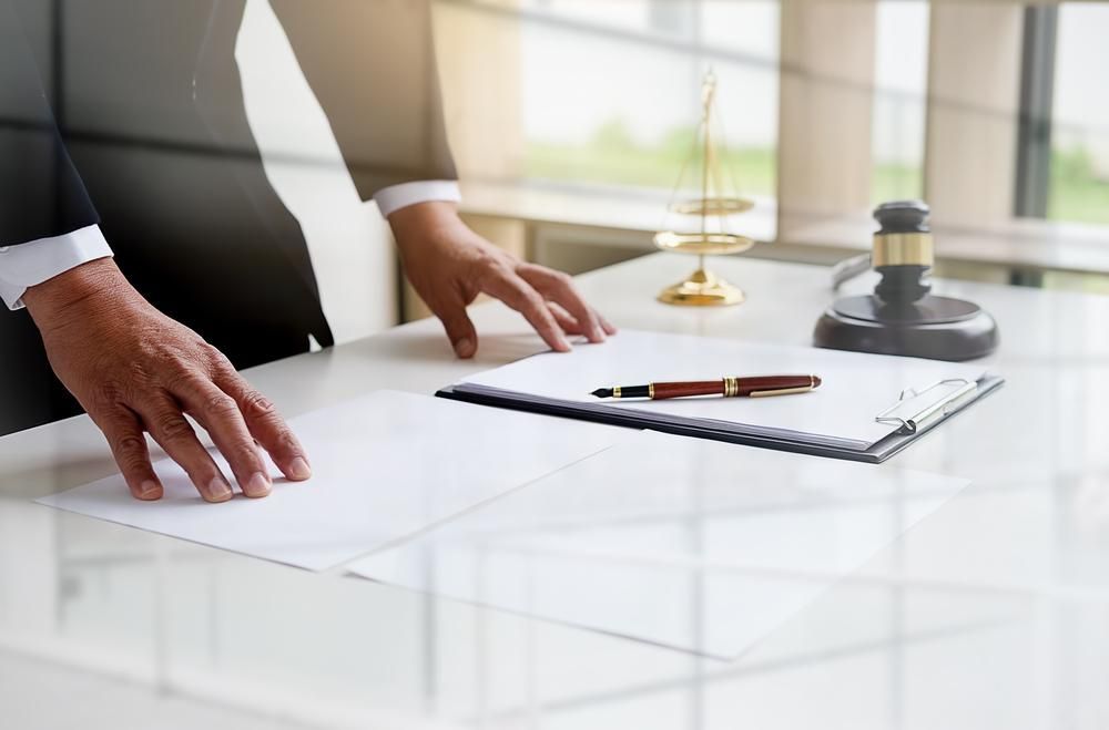 A Man in a Suit is Standing at a Table With Papers and a Judge 's Gavel — Olympus Lawyers In Ballarat Central, VIC